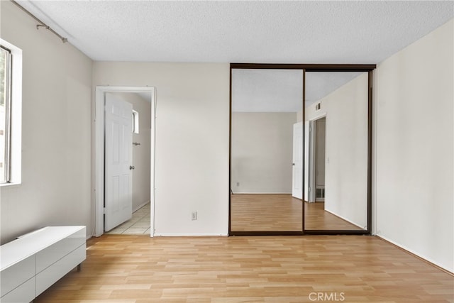 unfurnished bedroom featuring light hardwood / wood-style flooring, a textured ceiling, and a closet