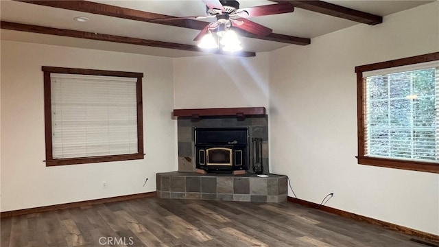 unfurnished living room with beamed ceiling, dark wood-type flooring, a wood stove, and ceiling fan