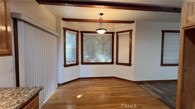 unfurnished dining area featuring light hardwood / wood-style floors and beamed ceiling