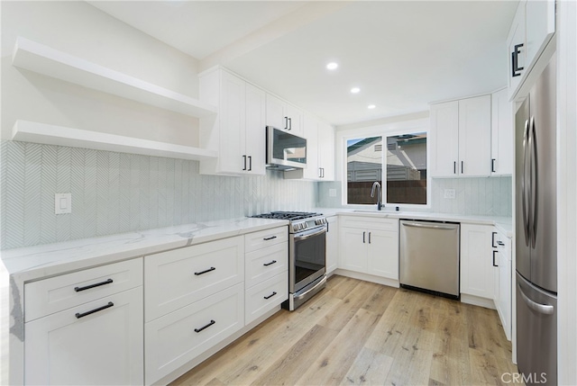 kitchen with white cabinets, light stone counters, appliances with stainless steel finishes, light hardwood / wood-style flooring, and sink