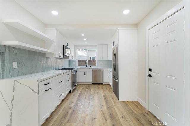 kitchen with white cabinetry, light stone counters, stainless steel appliances, and light wood-type flooring