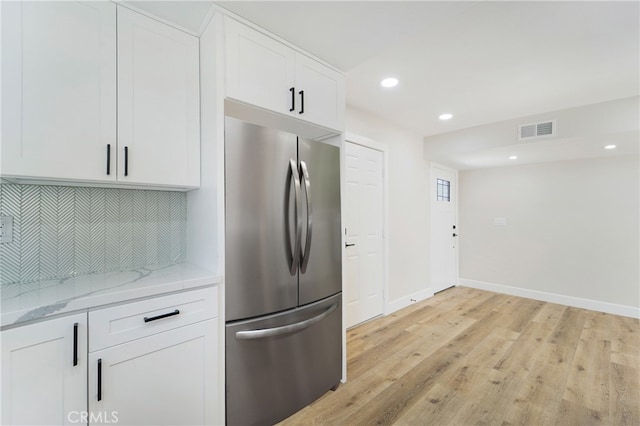 kitchen with tasteful backsplash, white cabinetry, stainless steel refrigerator, light hardwood / wood-style floors, and light stone counters