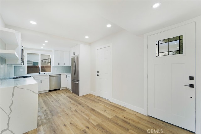 kitchen featuring white cabinets, tasteful backsplash, light stone countertops, light hardwood / wood-style floors, and stainless steel appliances