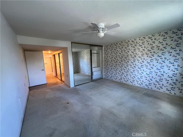 unfurnished bedroom with a textured ceiling, carpet floors, a ceiling fan, a closet, and wallpapered walls