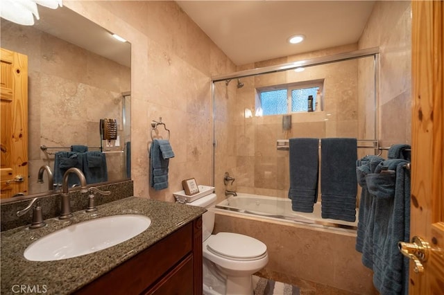 full bathroom featuring vanity, toilet, tile walls, and bath / shower combo with glass door