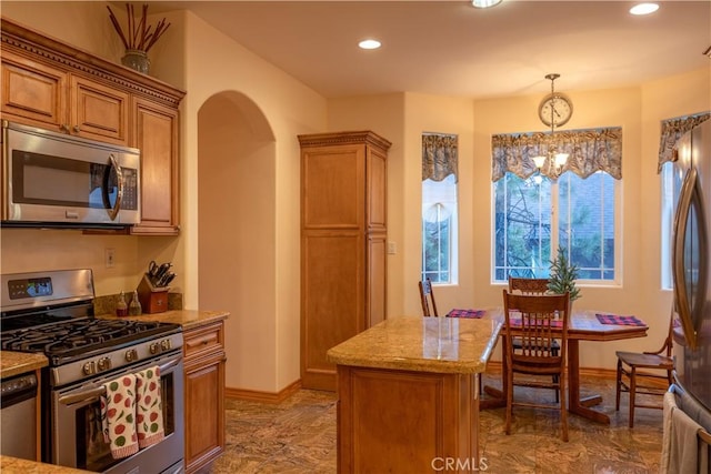 kitchen with light stone countertops, a center island, stainless steel appliances, an inviting chandelier, and pendant lighting