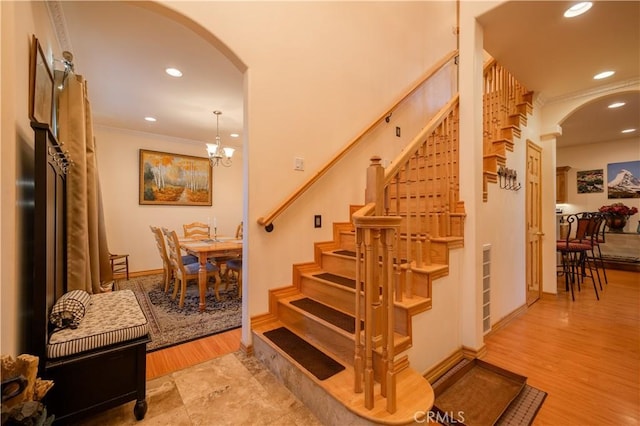 staircase featuring crown molding, an inviting chandelier, and hardwood / wood-style flooring