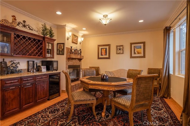 dining area featuring wine cooler, crown molding, light hardwood / wood-style flooring, and indoor wet bar