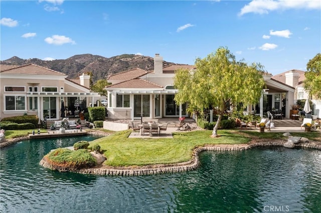 back of property featuring a yard, a sunroom, a water and mountain view, and a patio