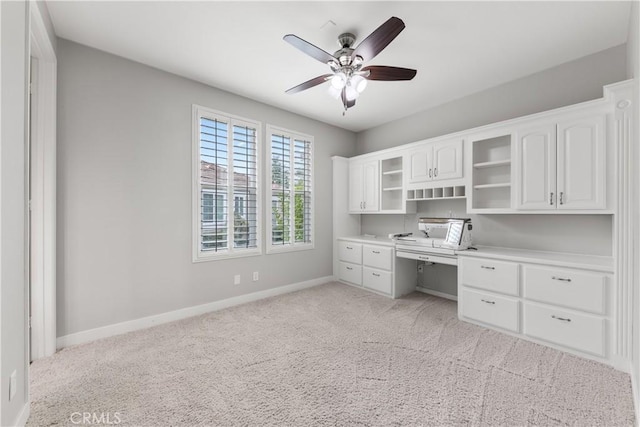 unfurnished office featuring ceiling fan, built in desk, and light carpet