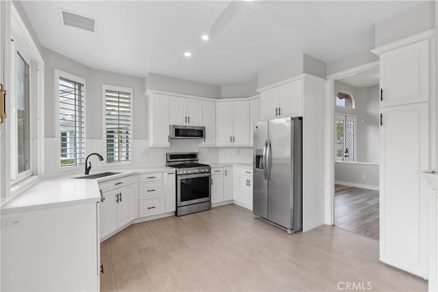 kitchen featuring light wood-type flooring, tasteful backsplash, stainless steel appliances, sink, and white cabinets