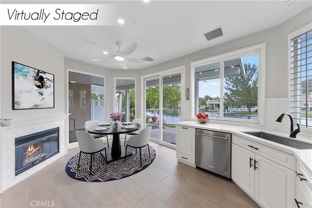 kitchen with dishwasher, white cabinets, sink, ceiling fan, and a fireplace