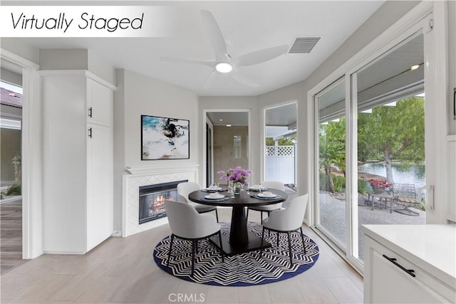 dining room featuring a tiled fireplace, a wealth of natural light, a water view, and ceiling fan