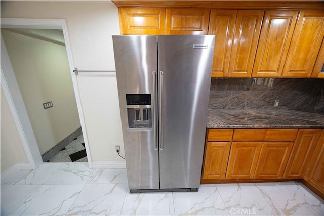 kitchen featuring stainless steel refrigerator with ice dispenser, backsplash, and dark stone countertops