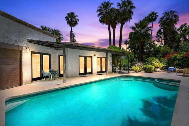 pool at dusk with ceiling fan, a patio, and french doors