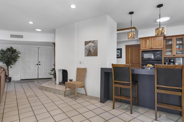 kitchen featuring decorative light fixtures, black microwave, french doors, light tile patterned floors, and a breakfast bar