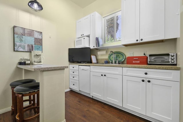 kitchen with white appliances, dark wood-type flooring, white cabinetry, a kitchen breakfast bar, and sink