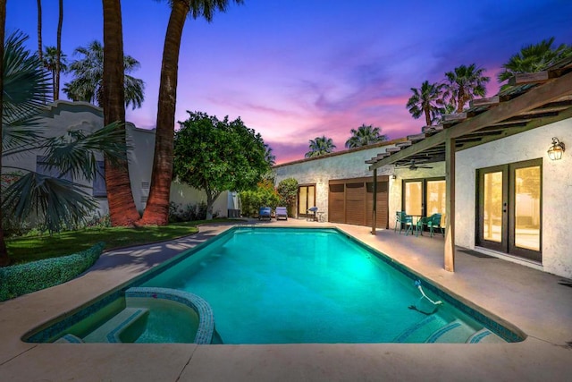 pool at dusk featuring a patio area and an in ground hot tub