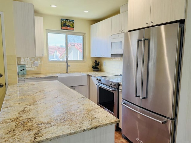 kitchen featuring stainless steel appliances, light stone counters, a sink, and tasteful backsplash