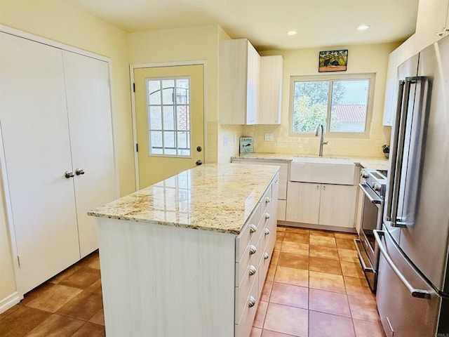 kitchen featuring light tile patterned floors, stainless steel appliances, decorative backsplash, a sink, and light stone countertops