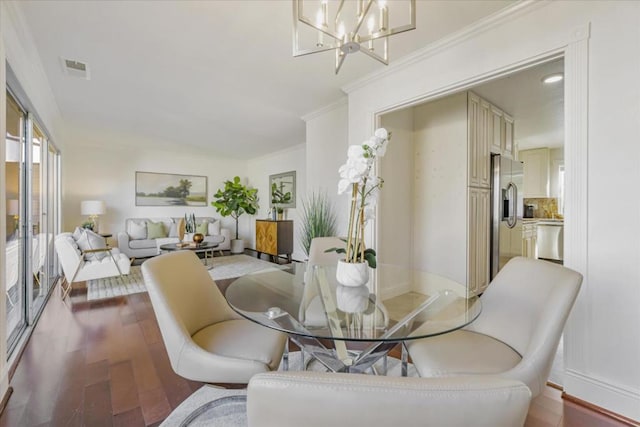 dining space with wood-type flooring, an inviting chandelier, and ornamental molding