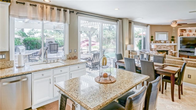 kitchen with dishwasher, a fireplace, white cabinetry, ceiling fan, and light stone counters