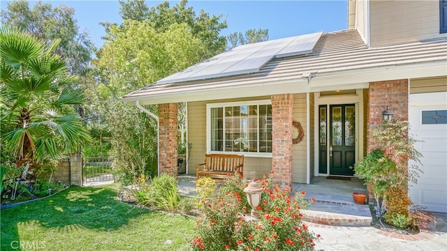 doorway to property with a yard, a garage, solar panels, and a porch