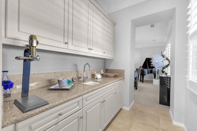 kitchen featuring light stone countertops, ornamental molding, sink, light tile patterned floors, and white cabinetry