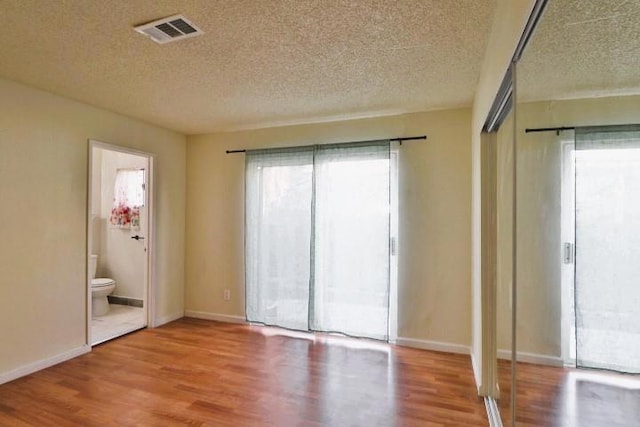 unfurnished bedroom with connected bathroom, wood-type flooring, and a textured ceiling