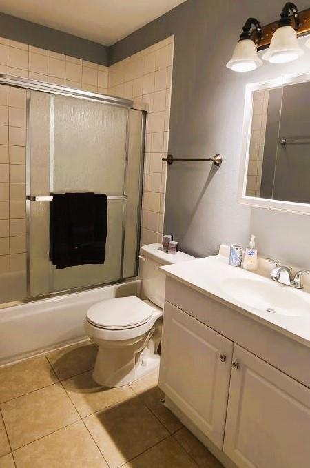 full bathroom featuring vanity, tile patterned floors, shower / bath combination with glass door, and toilet