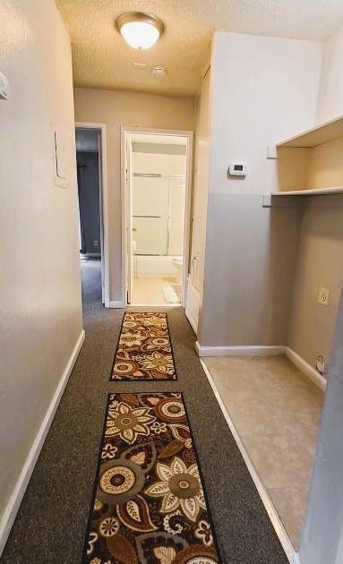 hallway with a textured ceiling and dark colored carpet