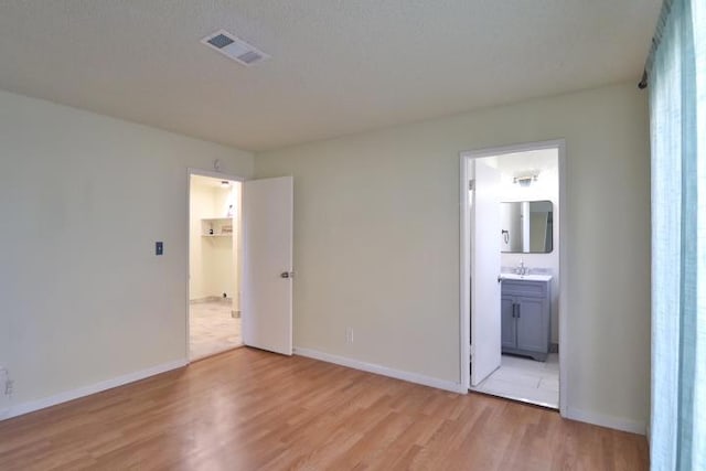 unfurnished bedroom with connected bathroom, a textured ceiling, and light wood-type flooring