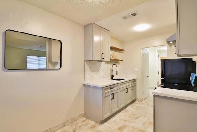 kitchen featuring sink, tasteful backsplash, a textured ceiling, black fridge, and exhaust hood