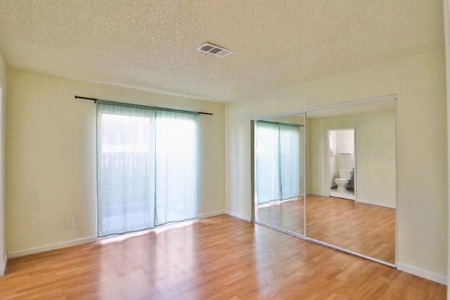 unfurnished bedroom with ensuite bath, wood-type flooring, a closet, and a textured ceiling