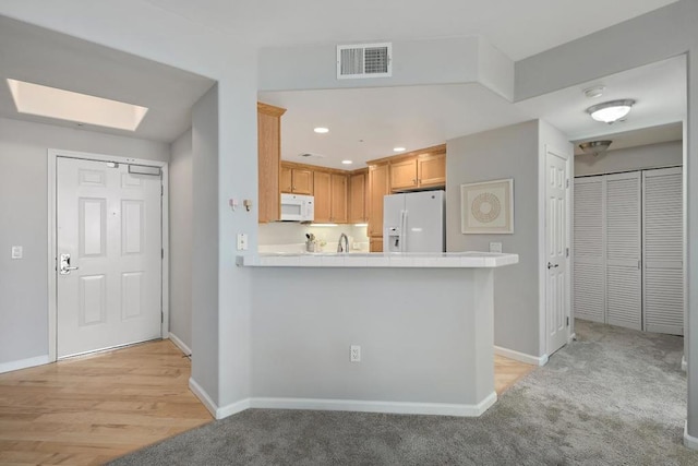 kitchen with kitchen peninsula, light brown cabinets, light carpet, white appliances, and a skylight