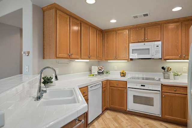 kitchen with sink, white appliances, light hardwood / wood-style flooring, and tile counters