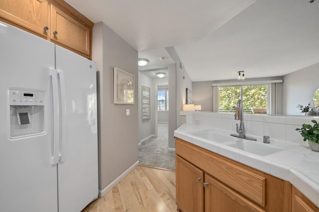 kitchen featuring sink, white refrigerator with ice dispenser, light hardwood / wood-style floors, and tile countertops