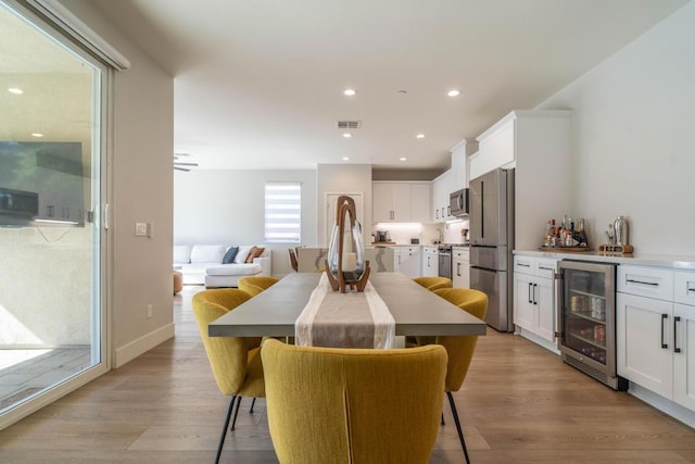 dining room with ceiling fan, light hardwood / wood-style floors, beverage cooler, and bar area