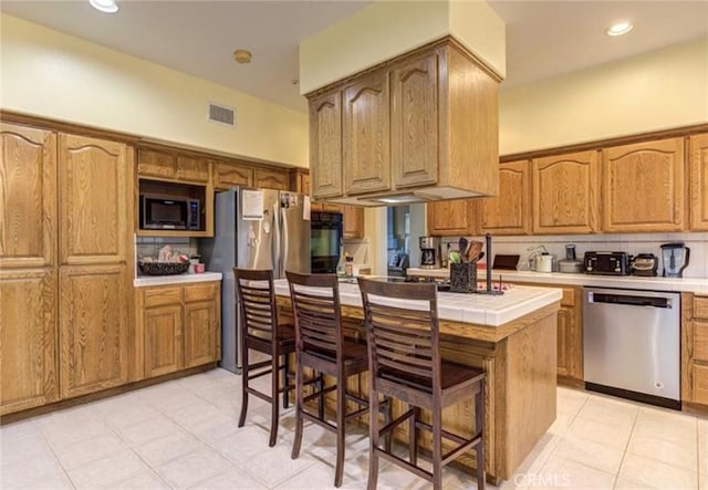 kitchen with tile countertops, a center island, a kitchen breakfast bar, light tile patterned floors, and stainless steel appliances