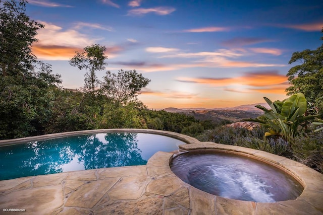 pool at dusk with an in ground hot tub