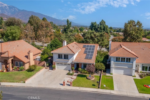 view of front of house featuring a mountain view, solar panels, a garage, and a front lawn