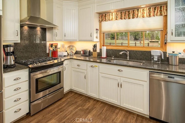 kitchen featuring appliances with stainless steel finishes, wall chimney exhaust hood, white cabinets, and dark stone counters