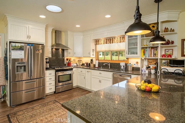 kitchen featuring appliances with stainless steel finishes, wall chimney range hood, decorative light fixtures, and white cabinetry