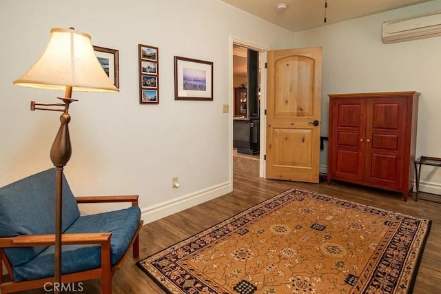sitting room featuring baseboards, a wall unit AC, and wood finished floors