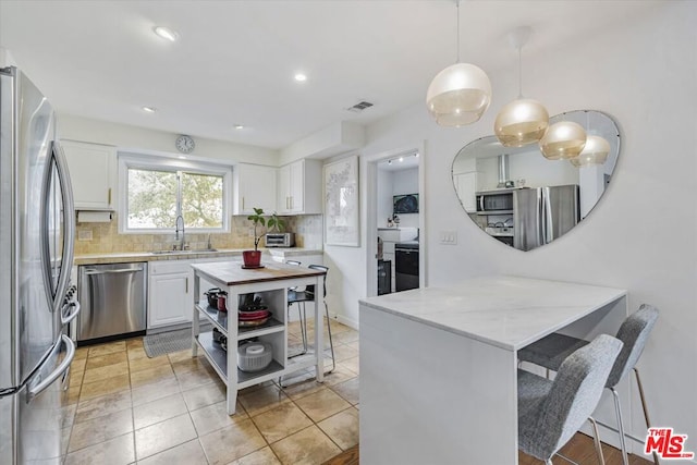 kitchen with sink, stainless steel appliances, decorative light fixtures, decorative backsplash, and white cabinets