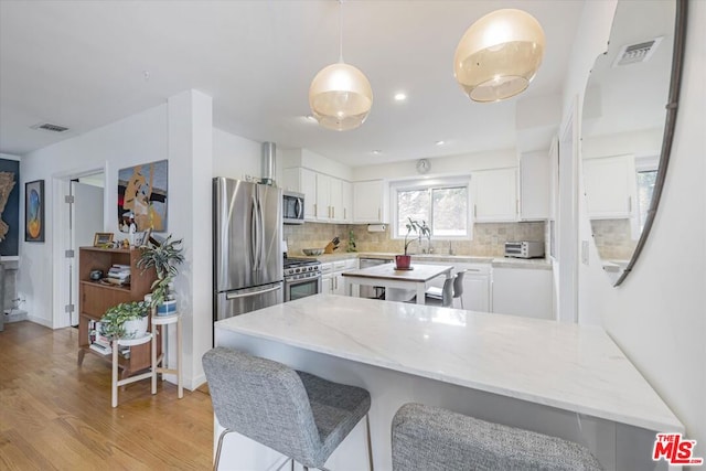 kitchen featuring light stone countertops, appliances with stainless steel finishes, light wood-type flooring, tasteful backsplash, and white cabinets