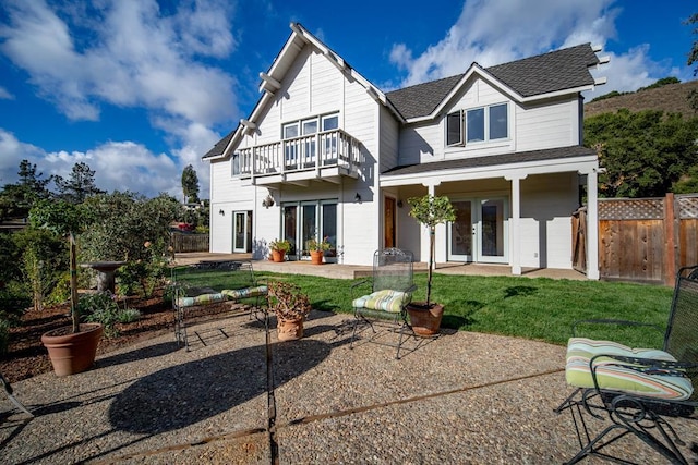 rear view of property with a lawn, french doors, a patio area, and a balcony