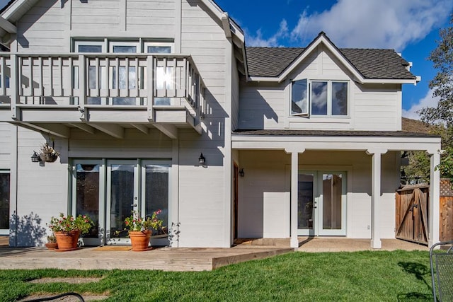 rear view of house featuring a lawn, french doors, and a balcony