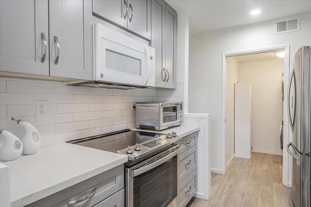 kitchen featuring tasteful backsplash, stainless steel appliances, gray cabinets, and light hardwood / wood-style floors