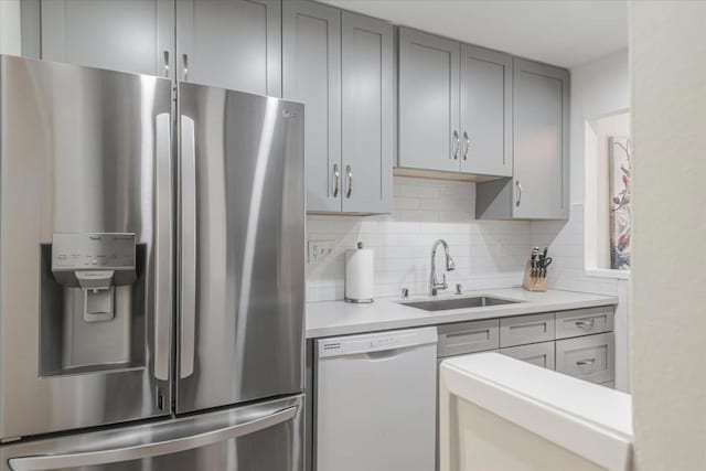 kitchen featuring gray cabinets, tasteful backsplash, dishwasher, sink, and stainless steel fridge with ice dispenser